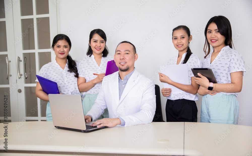 Portrait of confident asian medical team looking at a camera. Female nurses or students standing around male doctor or teacher in clinic office or hospital room Portrait of confident asian medical team looking at a camera. Female nurses or students standing around male doctor or teacher in clinic office or hospital room