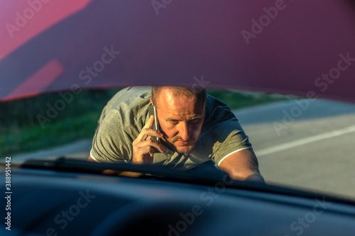 Shot of a young stressed man having trouble with his broken car looking in frustration at failed engine. Cropped shot of a young man with his broken down car on the side of a road. Man with broken car photo