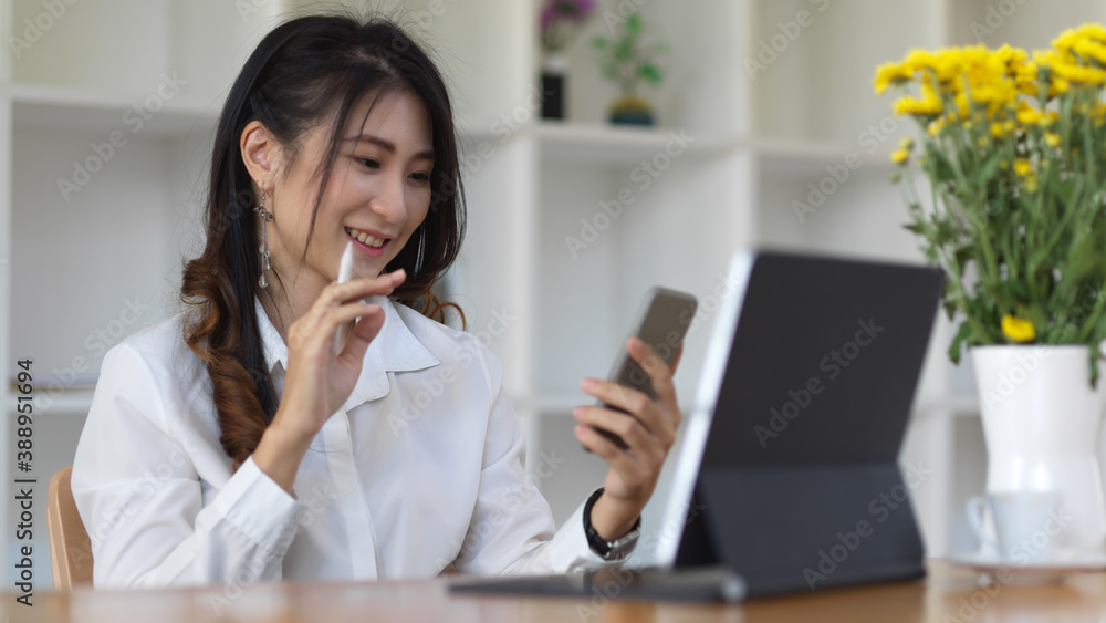 Female office worker holding her smartphone while working in office room Female office worker holding her smartphone while working in office room