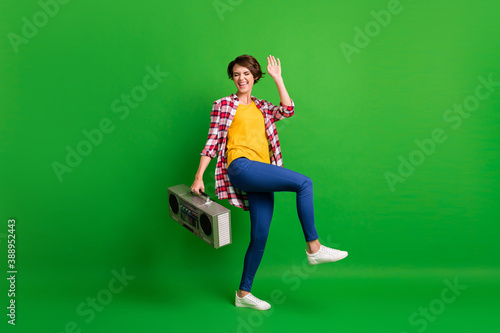 Full size photo of pretty positive lady dancing hold boombox wear jeans shirt sneakers isolated on green background