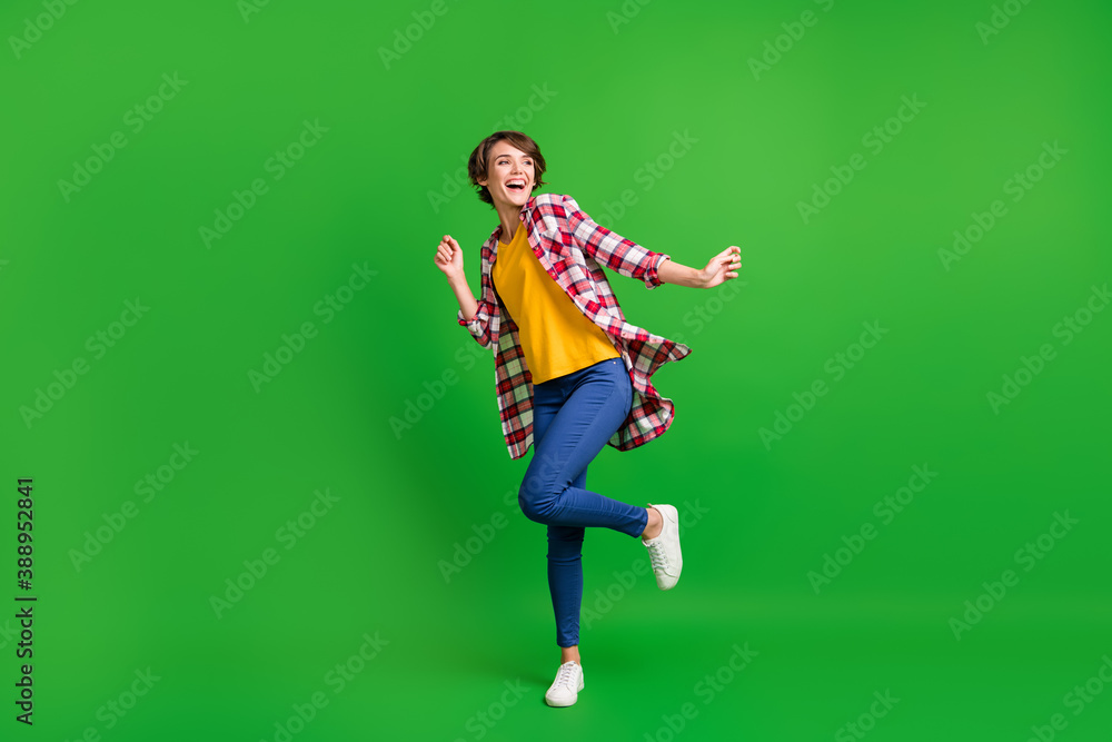 Full size photo of pretty cute lady dancing hands fists wear jeans shirt sneakers isolated on green color background Full size photo of pretty cute lady dancing hands fists wear jeans shirt sneakers isolated on green color background