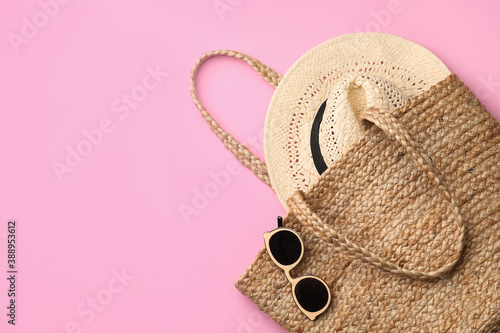 Elegant woman's straw bag with hat and sunglasses on pink background, top view. Space for text
