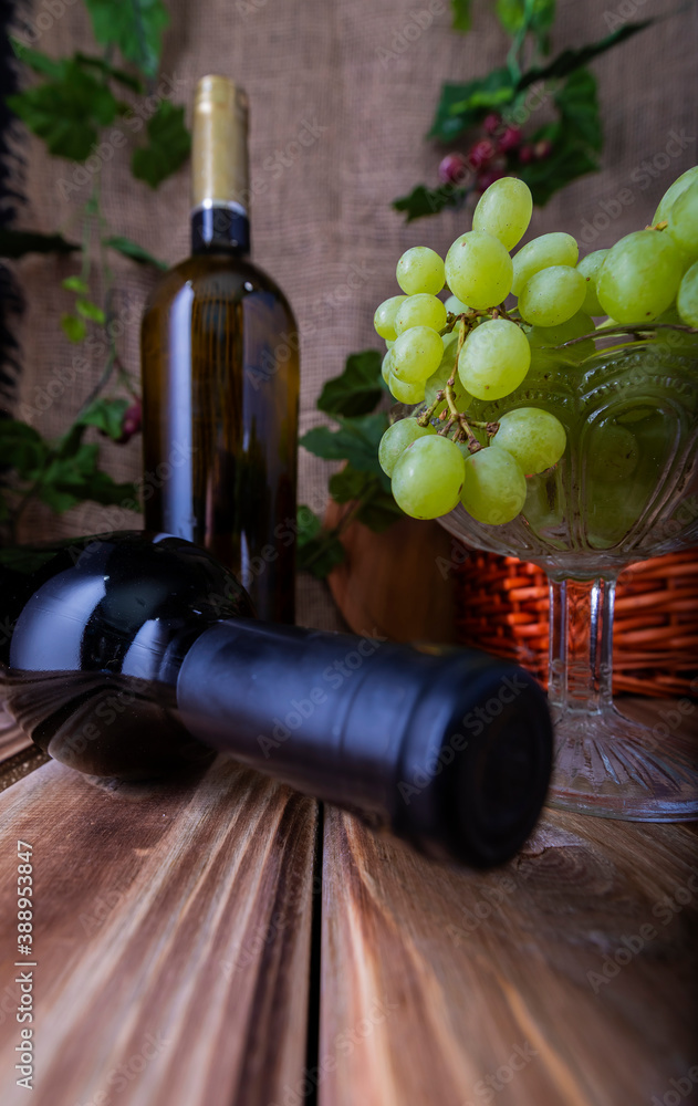 Obraz premium Two bottles of red and white wine on a wooden table with a bunch of grapes.