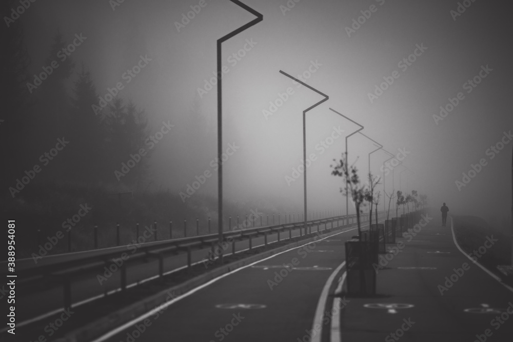 Dark road with double lines disappears into very thick fog and man