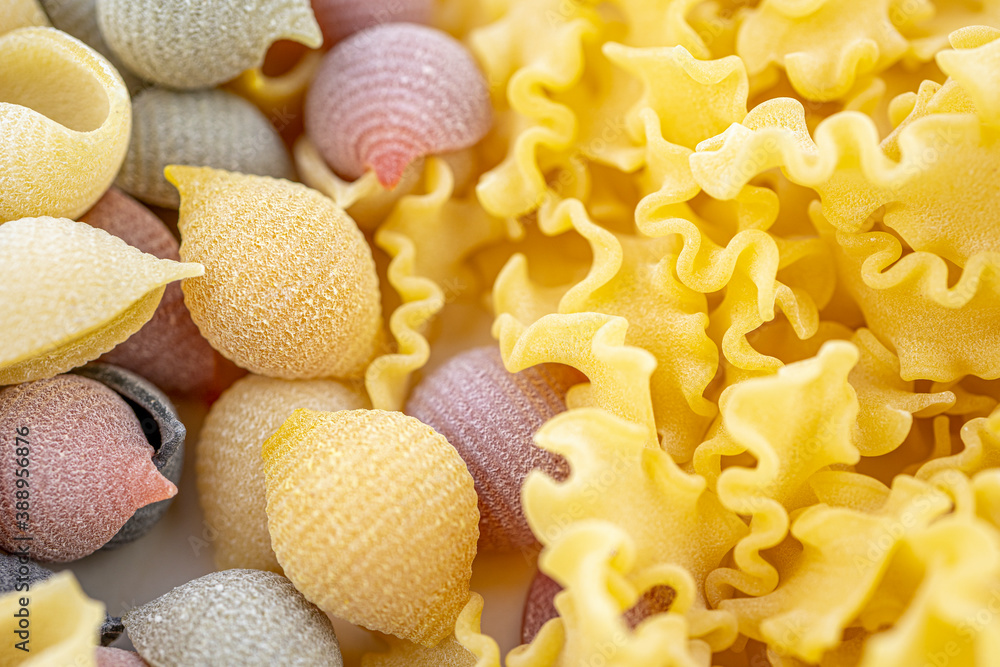 Colored Italian pasta in the shaped of seashells with yellow, pink, and ...