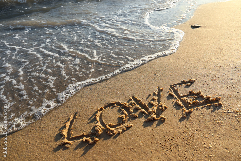 Fototapeta premium Word LOVE written on sandy beach near sea. Wedding concept