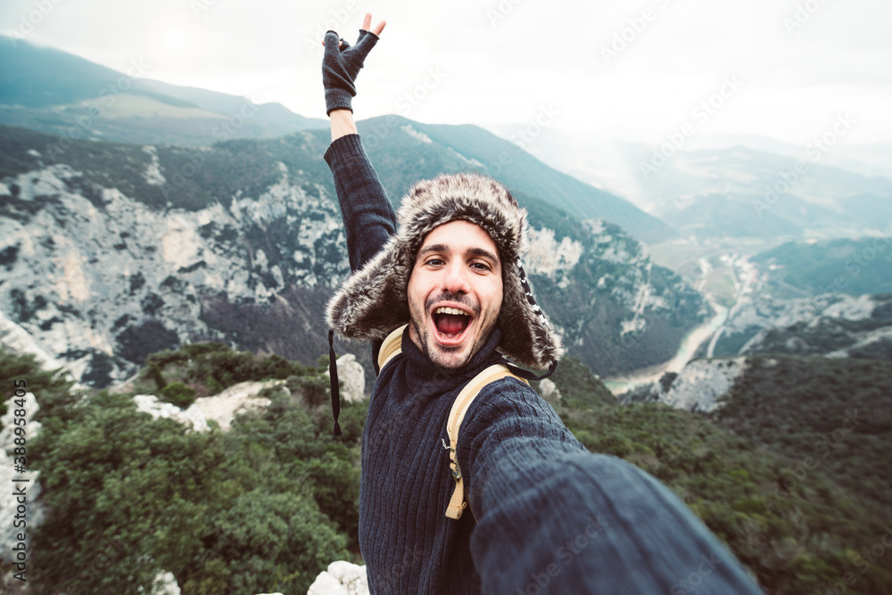 Handsome happy hiker taking a selfie on the top of the mountain - Smiling guy trekking outdoor at winter