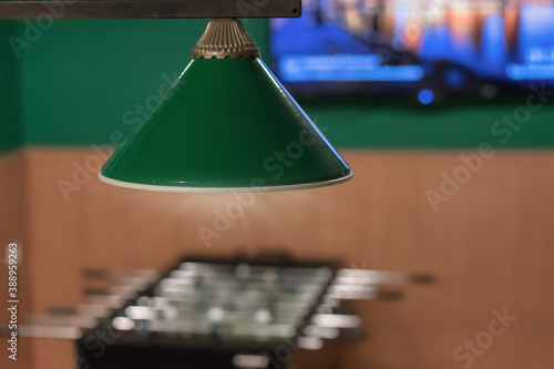 green lampshade with light hanging on ceiling of entertainment room with foosball table game photo