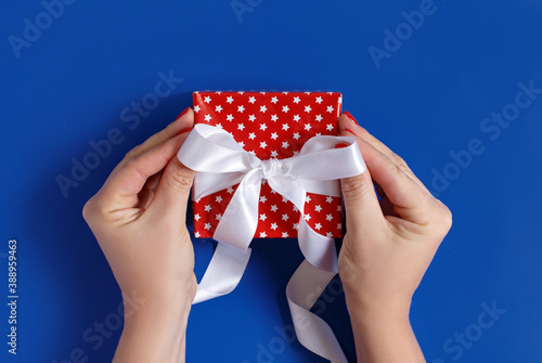 Hands tie a ribbon bow on a red gift box