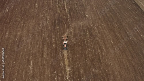 An aerial shot of a tractor pulling a spike harrow on a large agricultural field during daylight
