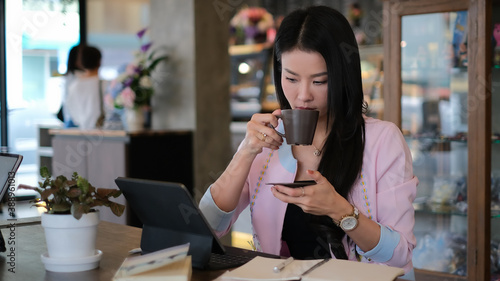 Beautiful young asian woman working on tablet and drinking coffee in the morning.