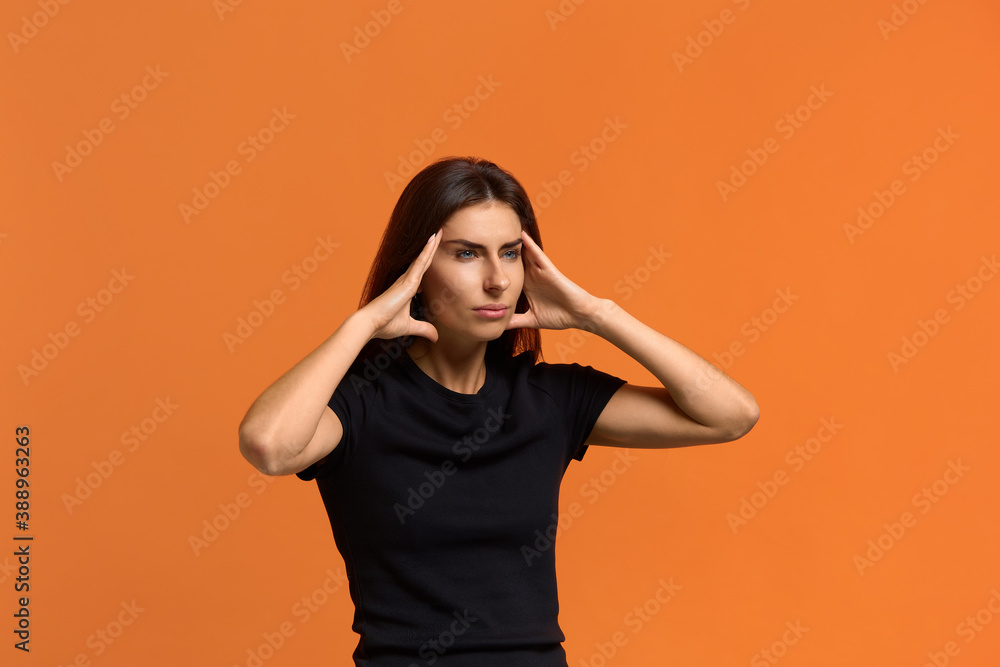 Leave me alone. Tired gloomy caucasian woman in black t-shirt holds hands on temples, has headache, feels exhausted and tension, looks sideways. Isolated over an orange background. Leave me alone. Tired gloomy caucasian woman in black t-shirt holds hands on temples, has headache, feels exhausted and tension, looks sideways. Isolated over an orange background.