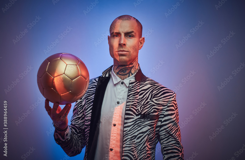 Plakat Tattooed serious man in stylish custom suit with jewellery poses in abstract background with golden ball.