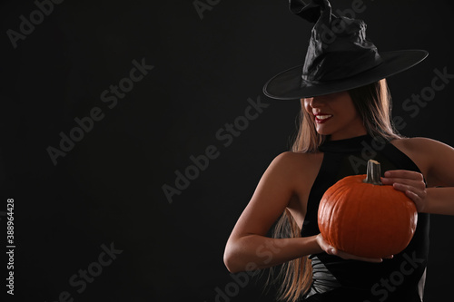 Young woman wearing witch costume with pumpkin on black background, space for text. Halloween party