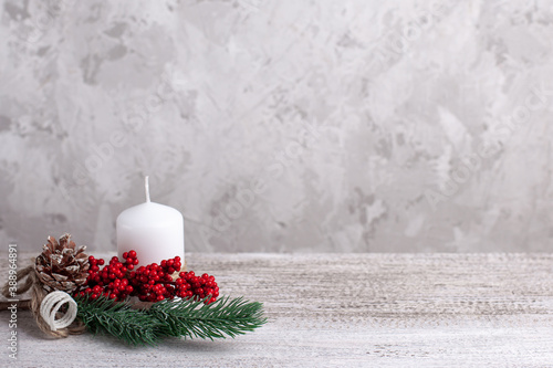 mock up of a white candle with a branch of a Christmas tree with decorations on a wooden table, card.