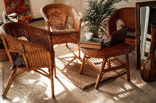 Luxurious and comfortable hotel room in daytime with bamboo chairs and table there are laptop and books with plant on it.