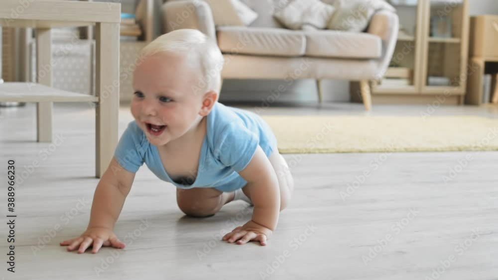 Wide shot of cute Caucasian toddler wearing blue bodysuit crawling around the room and laughing Wide shot of cute Caucasian toddler wearing blue bodysuit crawling around the room and laughing