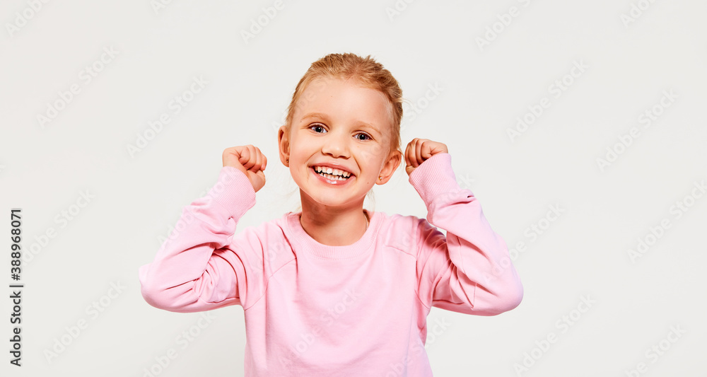 Happy smiling beautiful excited little girl wearing pink sweatshirt hold hands up isolated on a white background looking at camera. Free space for advertisement. Happy smiling beautiful excited little girl wearing pink sweatshirt hold hands up isolated on a white background looking at camera. Free space for advertisement.