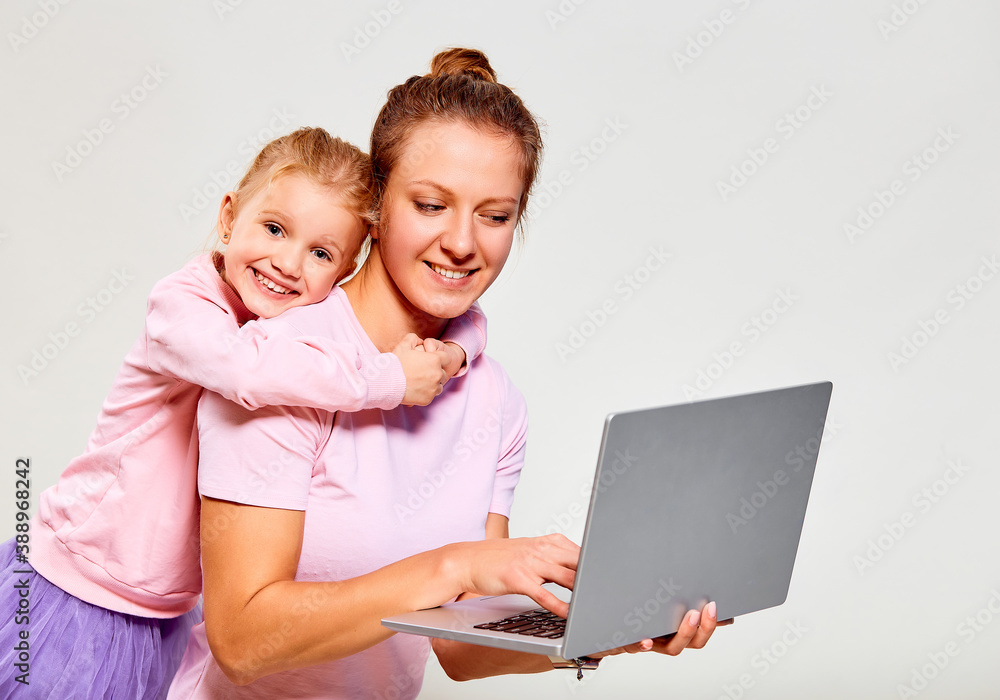 Closeup portrait of сute girl 4-5 year old and her mother in pink clothes, using laptop on gray background. Free space for advertisement. Closeup portrait of сute girl 4-5 year old and her mother in pink clothes, using laptop on gray background. Free space for advertisement.
