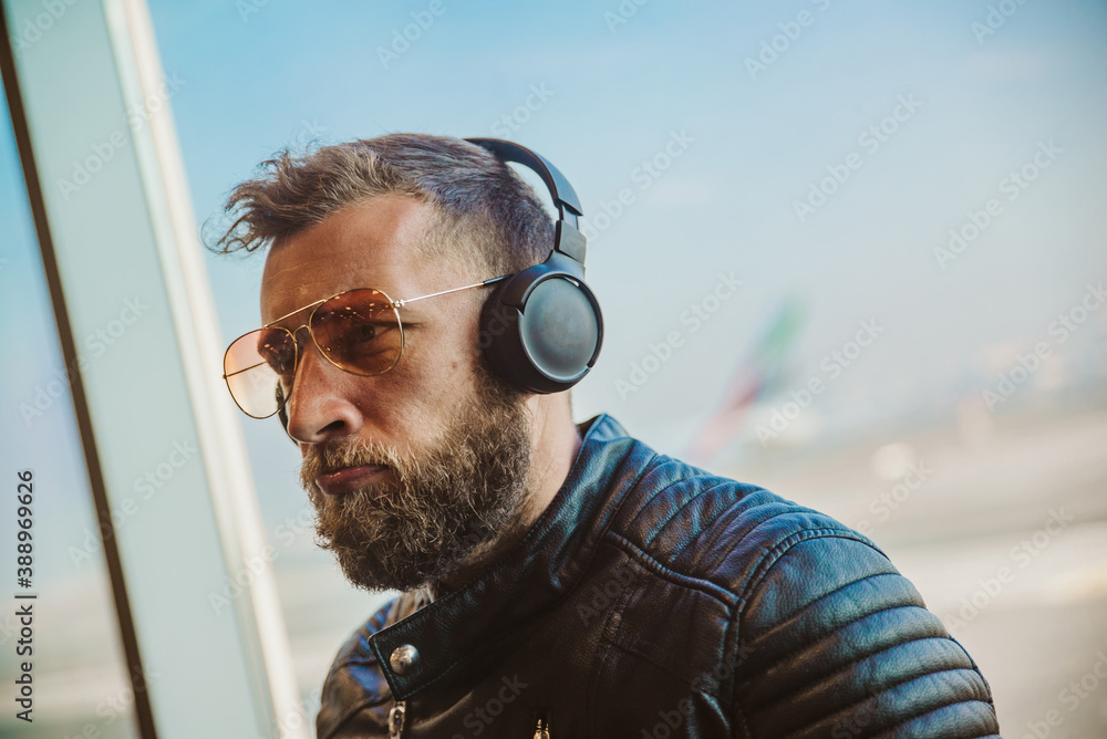 Φωτογραφία A portrait of a young handsome guy at the airport, who wears sunglasses and enjoys listening to music