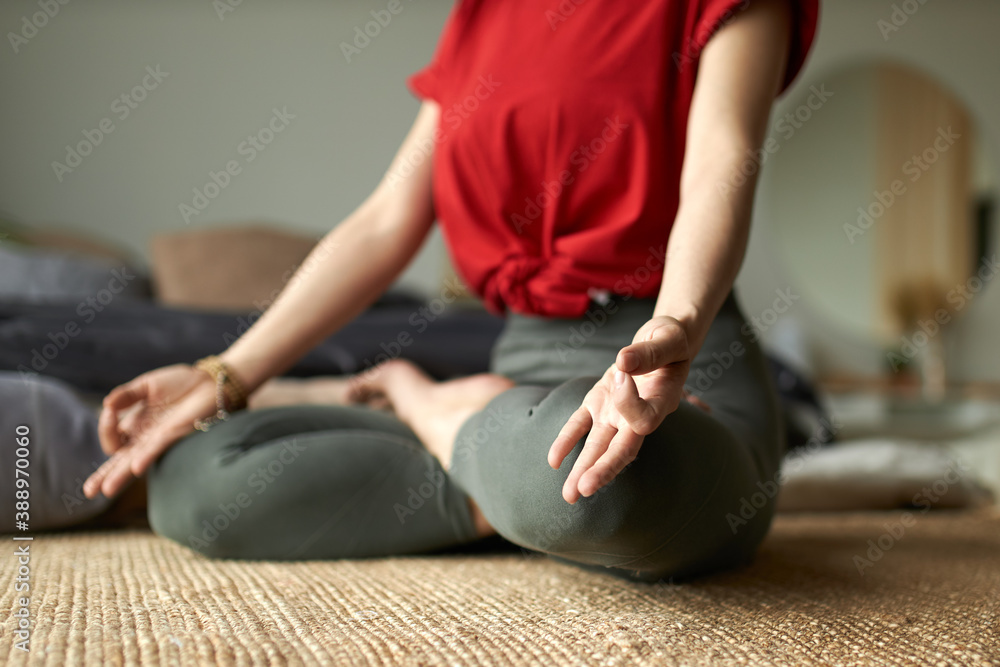 Zen, peace, concentration and relaxation concept. Cropped shot of unrecognizable female sitting barefoot in padmasana, meditating in the morning during yoga, her thumb and index finger making circle