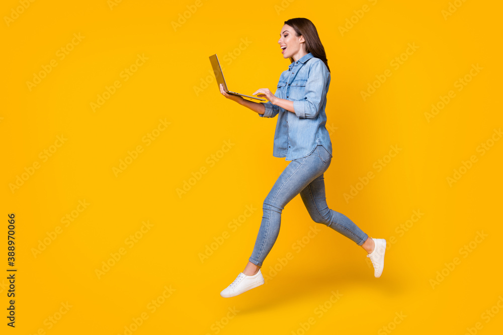 Full length body size profile side view of her she nice attractive slim fit cheerful glad girl jumping walking using laptop watch tutorial isolated bright vivid shine vibrant yellow color background Full length body size profile side view of her she nice attractive slim fit cheerful glad girl jumping walking using laptop watch tutorial isolated bright vivid shine vibrant yellow color background