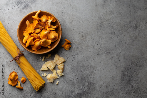 Wild forest mushrooms chanterelles in wooden bowl, raw pasta spaghetti and parmesan. Seasonal autumn food, ingredients for cooking fresh chanterelles pasta. Copy space, food background top view