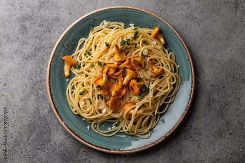 Pasta spaghetti with wild forest mushrooms chanterelles on plate. Seasonal autumn dish on rustic concrete background from above. Meal with aromatic fall chanterelles