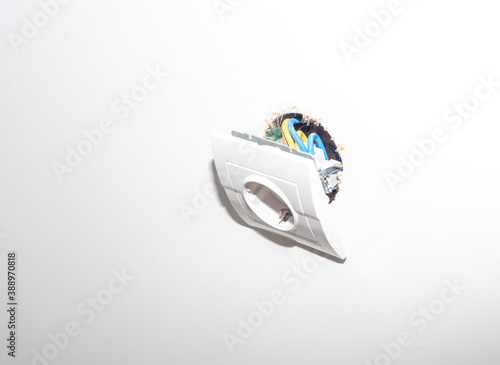 Broken electric socket torn from white wall background