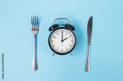 Top view alarm clock with knife and fork on blue background. Intermittent fasting, Ketogenic dieting, weight loss, meal plan and healthy food concept
