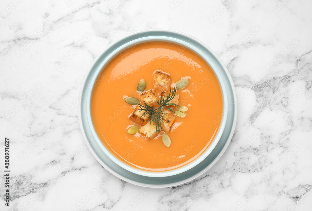 Tasty creamy pumpkin soup with croutons, seeds and dill in bowl on white marble table, top view