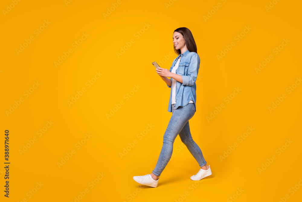 Full body profile photo of attractive cheerful lady good mood walk down street chatting telephone friends meeting wear casual denim shirt sneakers isolated vivid yellow color background Full body profile photo of attractive cheerful lady good mood walk down street chatting telephone friends meeting wear casual denim shirt sneakers isolated vivid yellow color background