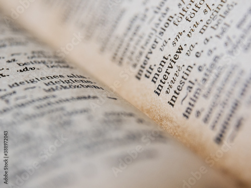 Close up of an open old book with white pages, and black letters on it, on a blurred background