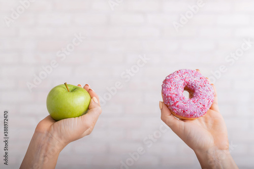 Donut and green apple in female hands. The concept of different eating habits. Thinness and obesity