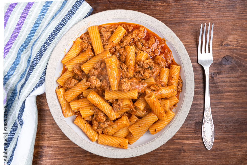 Cooking tortiglioni with onion and sausage ragout, pasta with sausage sauce with onions and tomato paste on a plate on a rustic wooden table, top view Cooking tortiglioni with onion and sausage ragout, pasta with sausage sauce with onions and tomato paste on a plate on a rustic wooden table, top view