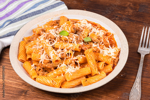 Cooking tortiglioni with onion and sausage ragout  pasta with sausage sauce with onions and tomato paste  sprinkled with tertum cheese on a plate on a rustic wooden table  top view