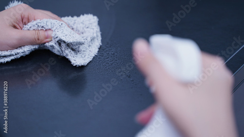 Woman housekeeper using rag and spraying bottle to clean the table surface.