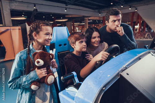 Boy is riding car in arcade. Family is cheering and helping.