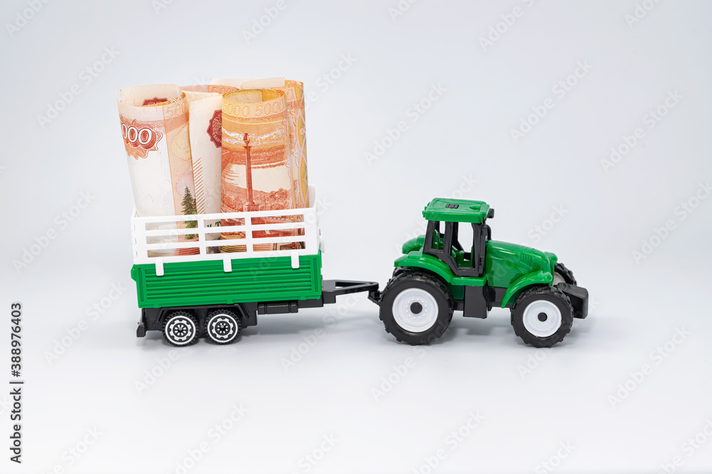 A toy green farm tractor carries five-thousand-ruble bills rolled into a tube in a trailer