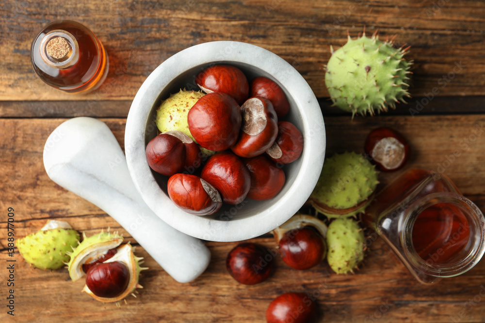 Mortar with pestle, chestnuts and essential oil on wooden table, flat lay Mortar with pestle, chestnuts and essential oil on wooden table, flat lay