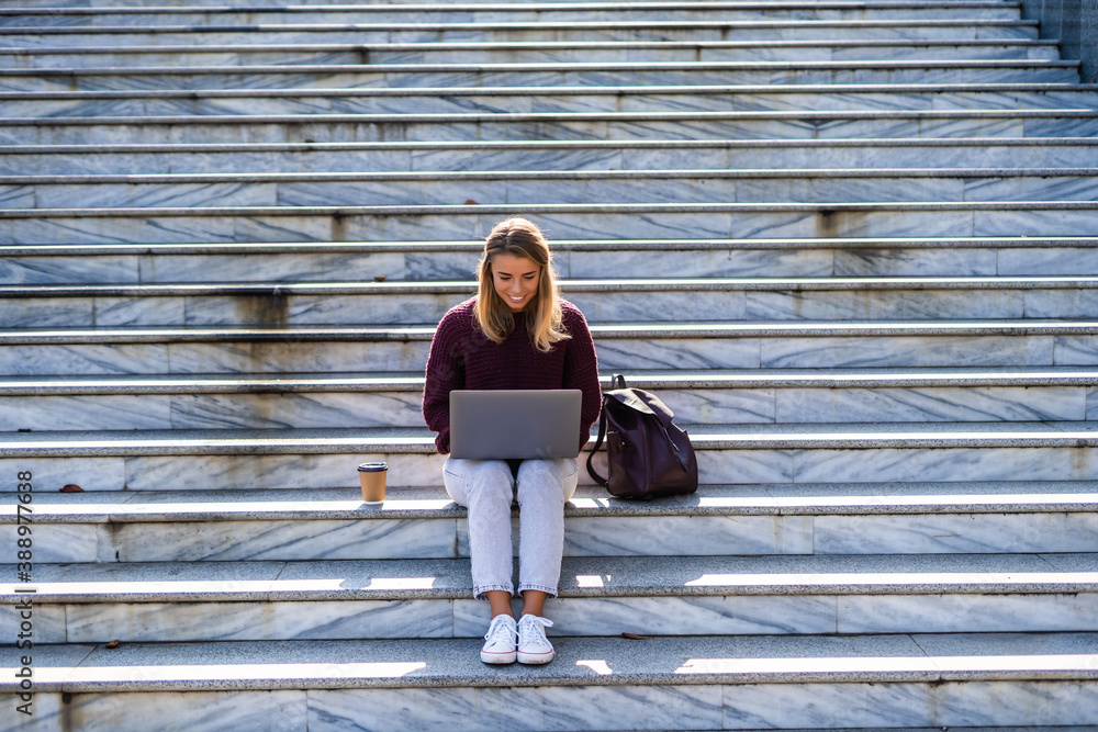 Portrait of a happy young woman sitting on the city stairs and using laptop outdoors Portrait of a happy young woman sitting on the city stairs and using laptop outdoors