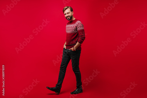 Full-length portrait of man in red sweater and black pants. Indoor photo of cheerful male model waiting for christmas.