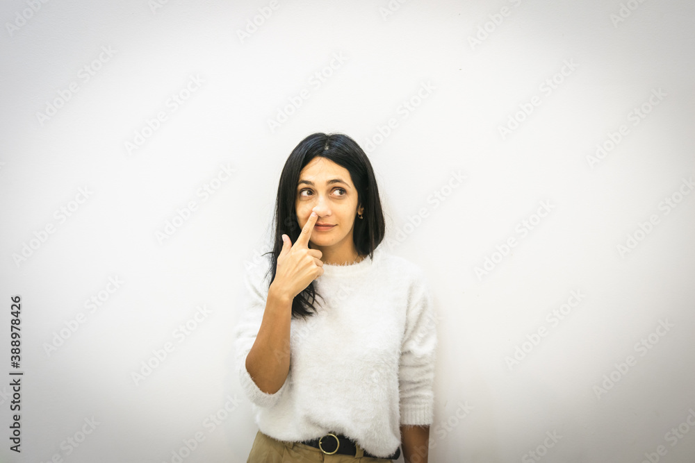 Young brunette caucasian woman puts finger to her right nose nostrils and looks to the side in white background. Silly bored and relaxed person at work. Young brunette caucasian woman puts finger to her right nose nostrils and looks to the side in white background. Silly bored and relaxed person at work.