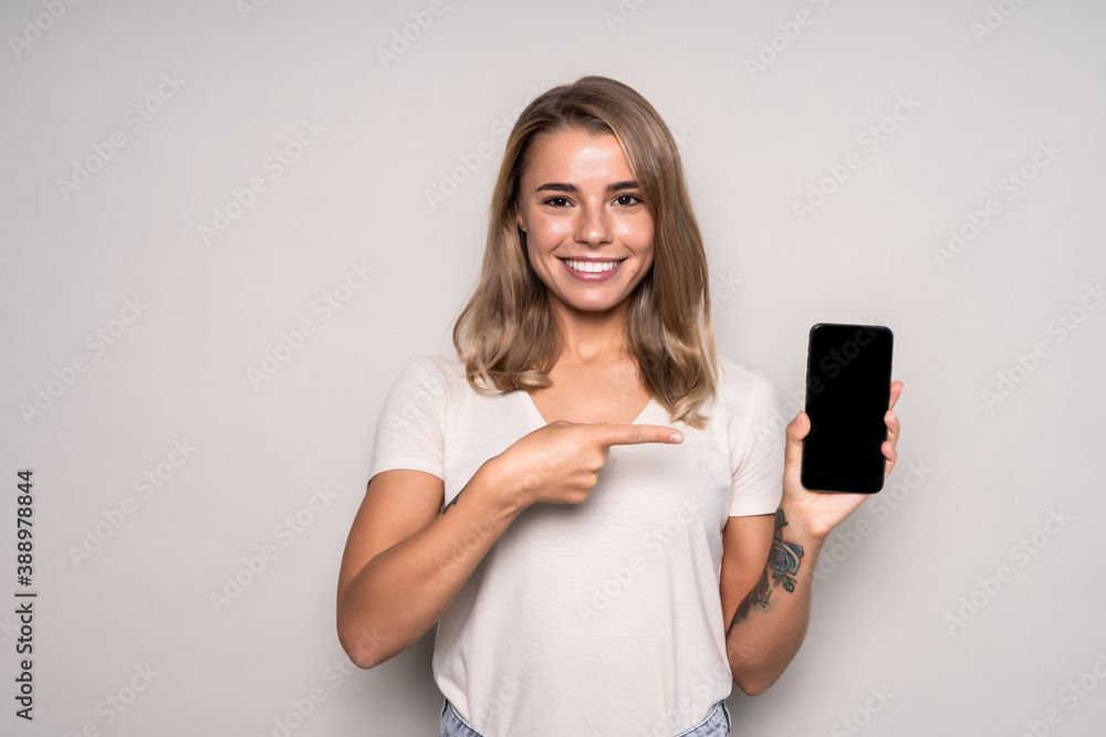 Joyful woman showing blank smartphone screen and looking at the camera over white background Joyful woman showing blank smartphone screen and looking at the camera over white background