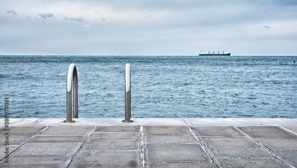 Obraz premium Concrete pier with steel ladder in the sea with ship