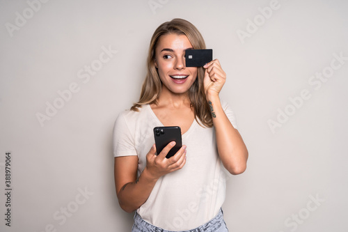 Cheerful excited young woman with mobile phone and credit card over white background
