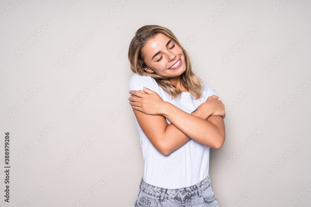Portrait of a pretty young woman hugging herself with eyes closed while standing isolated over white background Portrait of a pretty young woman hugging herself with eyes closed while standing isolated over white background