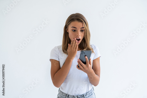 Portrait of a surprised attractive girl holding mobile phone and looking at camera isolated over white background