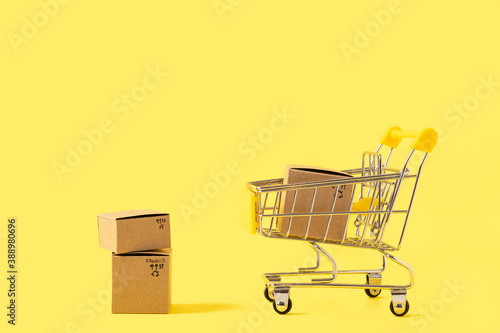 Toy shopping cart with boxes on yellow background. Copy space for text or design. Sale, discount, shopping and delivery concept. Consumer society trend.