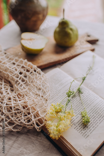 Summer rustic still life. Fresh ripe organic pears on wood board, an open book and a field flower. Retro style photo. Natural healthy lunch.
